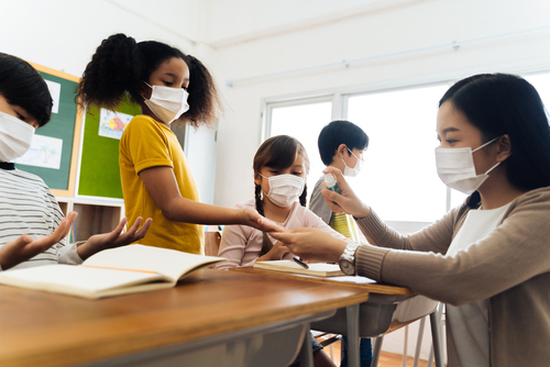 Group of students wearing masks surrounding masked teacher as they return to school after the COVID-19 pandemic